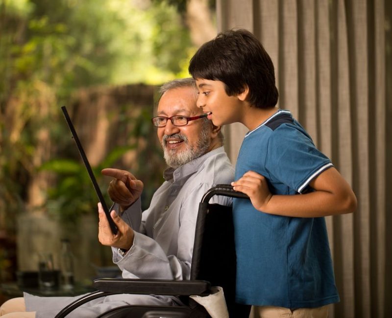 Grandson with disabled grandfather showing picture frame on wheelchair at home